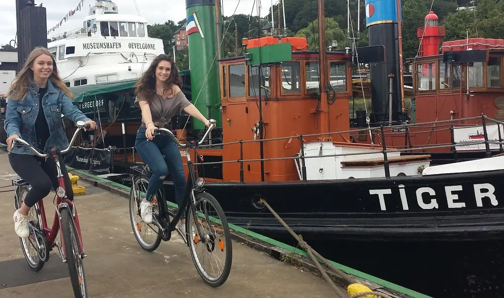 2 junge Frauen auf Verleih City Fahrrädern im Museumshafen Övelgönne. Ciy Fahrrad Ausleihe.