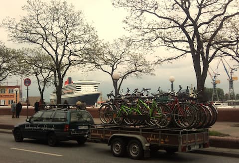 Fahrradtransport mit Tandems, Kinderrädern, City Bikes, Trekking Bikes u.a. Im Hintergrund die auslaufende Queen Mary 2.
